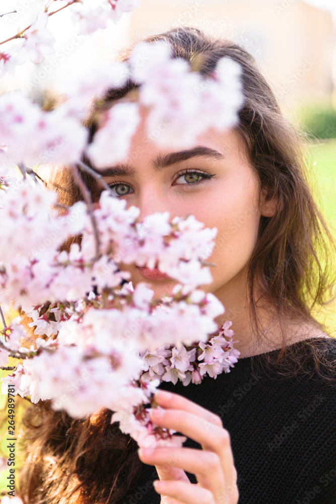 Fototapeta premium Portrait of girl hiding behind flowering branch