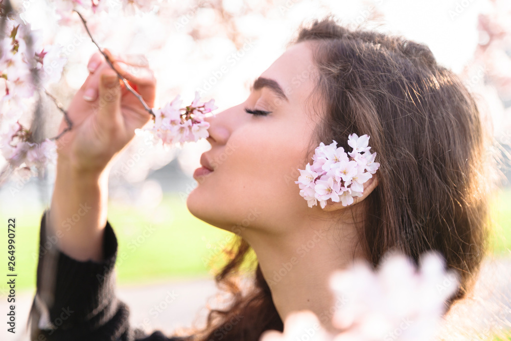 Obraz premium Girl smiles and sniffs flowers on blossom branch