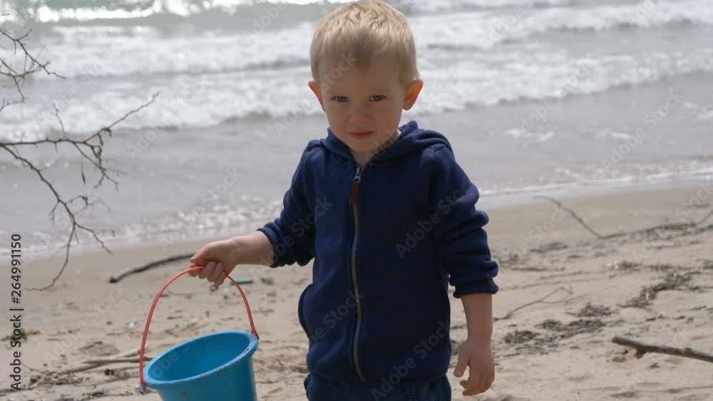 Child (little boy, toddler, two years old) is saying Hi. Beach, water, plastic kids bucket, emotional face Child (little boy, toddler, two years old) is saying Hi. Beach, water, plastic kids bucket, emotional face