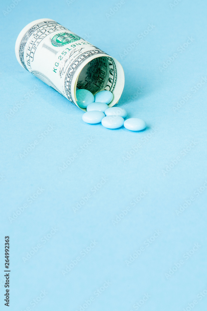 Money dollar rolled up with pills flowing out isolated on blue background, high costs of expensive medication concept. Copy space Money dollar rolled up with pills flowing out isolated on blue background, high costs of expensive medication concept. Copy space