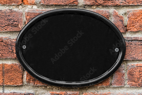 Blank black cast iron house number plate on a brick wall.