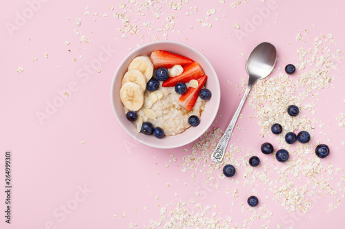 Bowl of oatmeal porridge with strawberry, blueberry and banana on pink pastel table top view. Healthy breakfast. Flat lay.