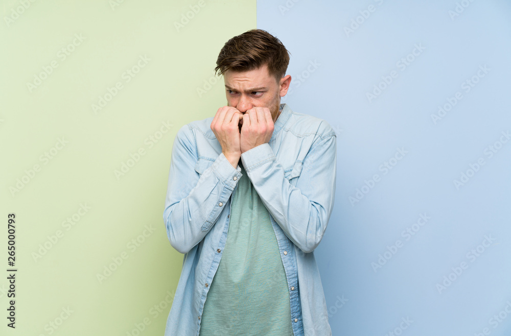Redhead man over colorful background nervous and scared putting hands to mouth Redhead man over colorful background nervous and scared putting hands to mouth