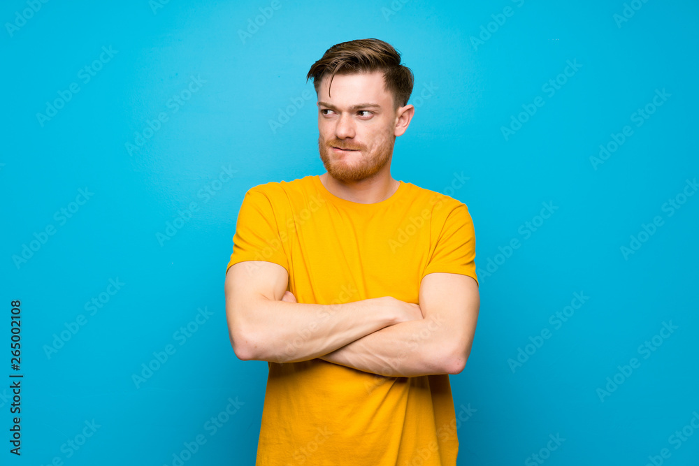 Redhead man over blue wall with confuse face expression Redhead man over blue wall with confuse face expression