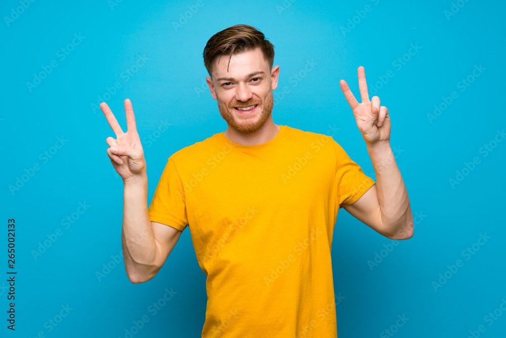 Fototapeta premium Redhead man over blue wall showing victory sign with both hands