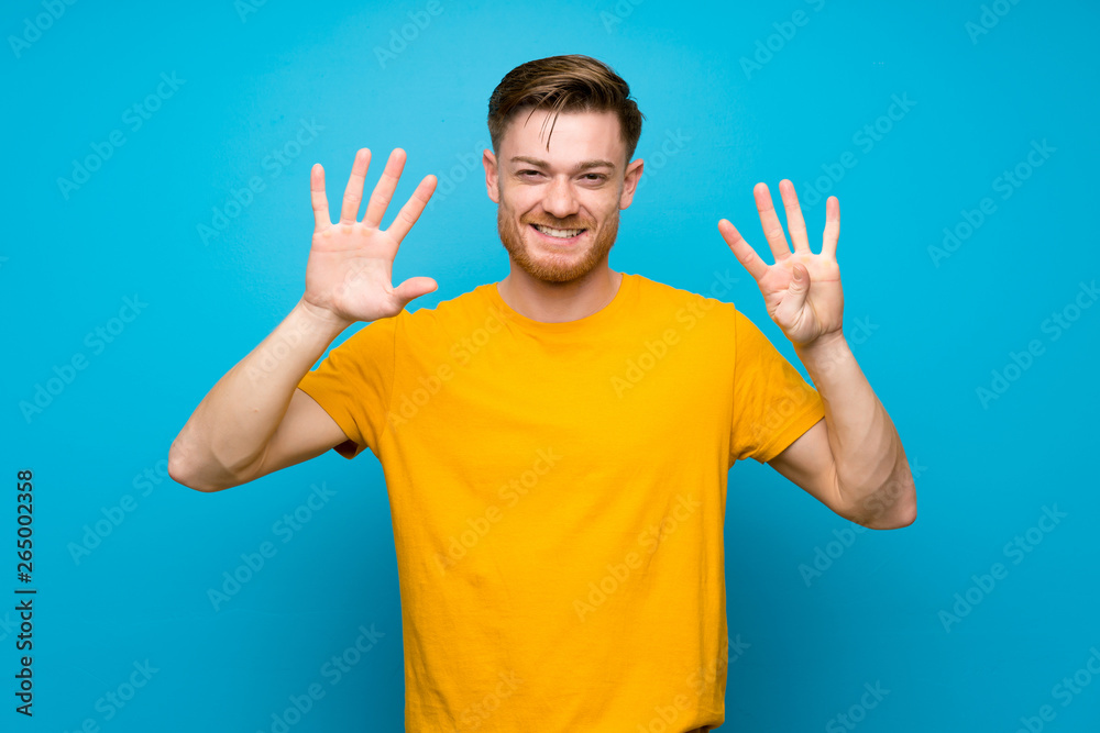 Redhead man over blue wall counting nine with fingers Redhead man over blue wall counting nine with fingers