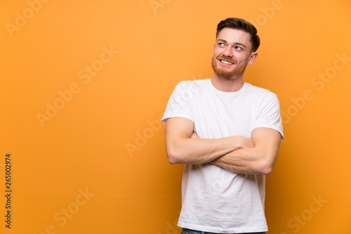 Redhead man over brown wall looking up while smiling
