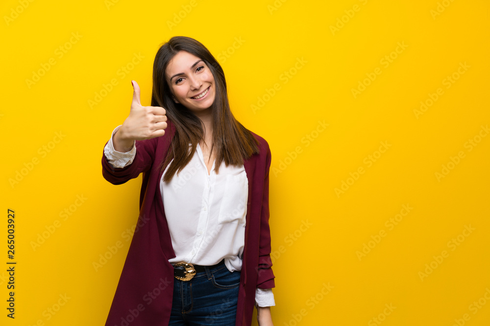 Young woman over yellow wall with thumbs up because something good has happened Young woman over yellow wall with thumbs up because something good has happened