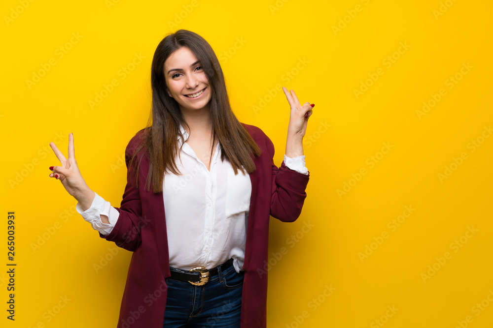 Young woman over yellow wall smiling and showing victory sign with both hands Young woman over yellow wall smiling and showing victory sign with both hands