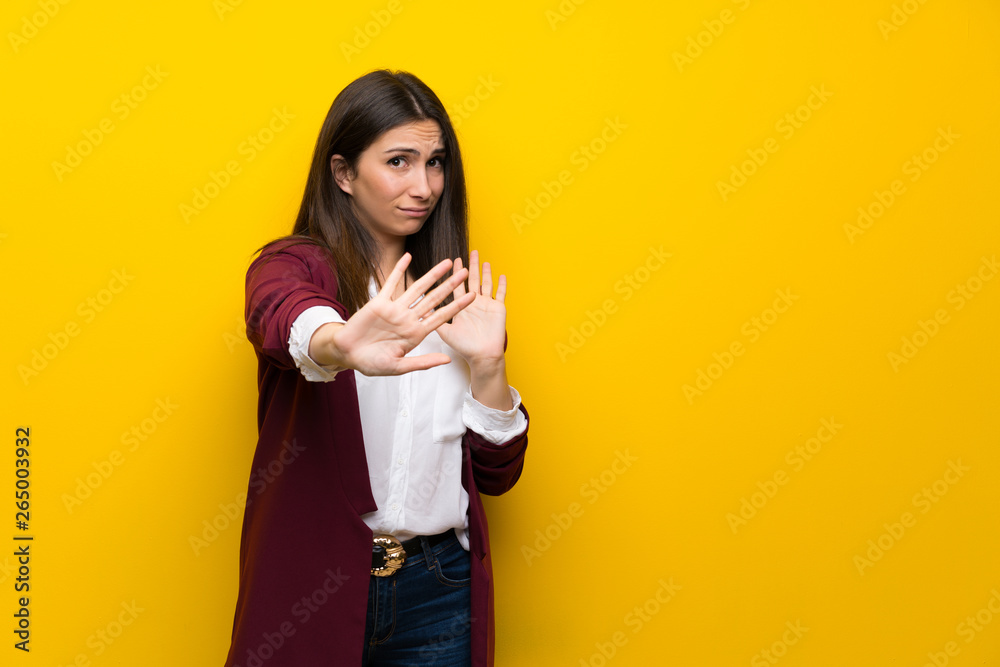 Young woman over yellow wall nervous and scared stretching hands to the front Young woman over yellow wall nervous and scared stretching hands to the front