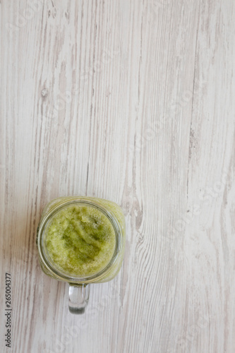 Green celery smoothie in a glass jar over white wooden surface, top view. Overhead, flat lay. Space for text.