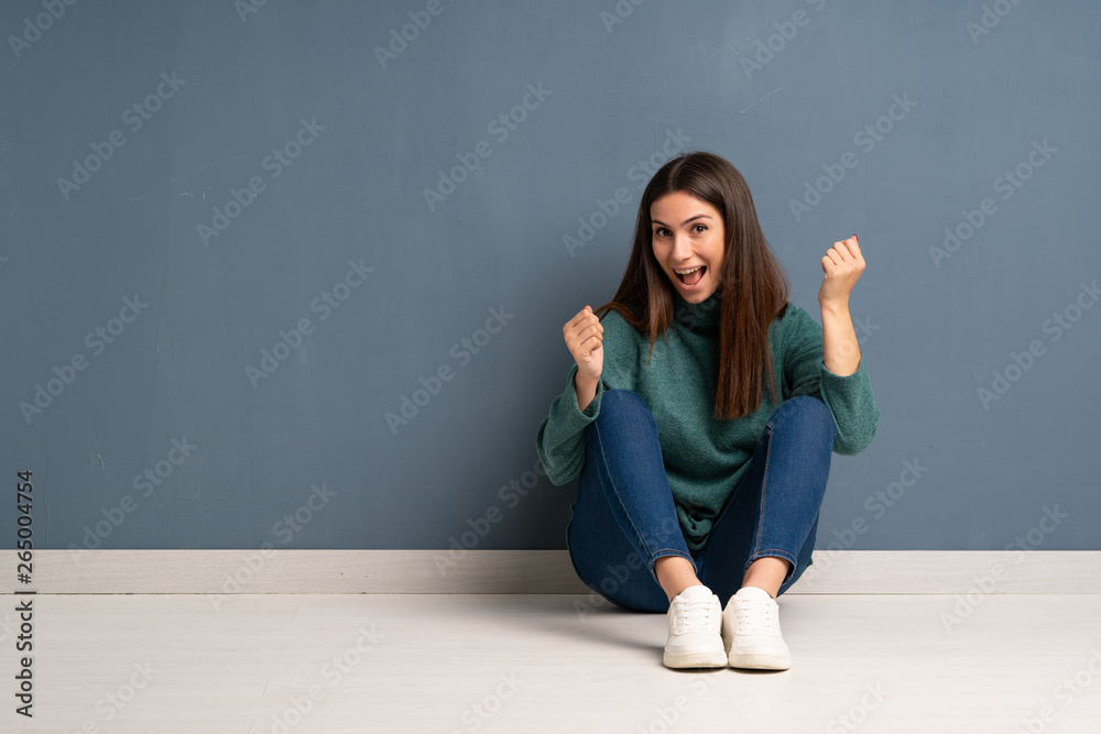 Young woman sitting on the floor celebrating a victory in winner position Young woman sitting on the floor celebrating a victory in winner position