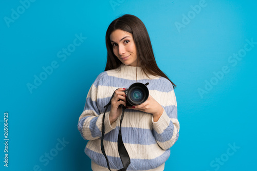 Young woman over blue wall holding a camera