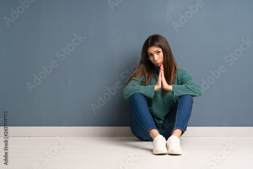 Young woman sitting on the floor keeps palm together. Person asks for something