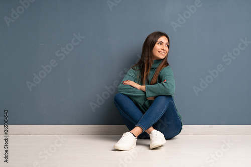Young woman sitting on the floor with arms crossed and happy