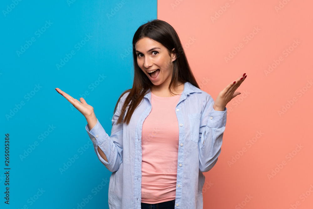 Young woman over pink and blue wall with surprise and shocked facial expression