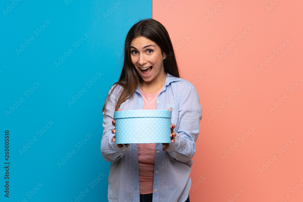 Young woman over pink and blue wall surprised because has been given a gift Young woman over pink and blue wall surprised because has been given a gift