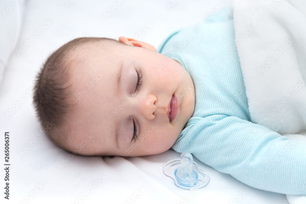 Baby sleeping with a pacifier aside. Light blue pajama and white bed sheets. Baby sleeping with a pacifier aside. Light blue pajama and white bed sheets.