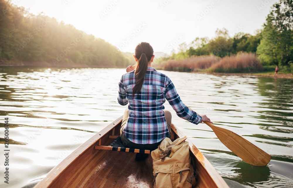 Rear view of travel girl paddling the canoe on the sunset lake. Paddling, canoeing, oar, boat, adventure Rear view of travel girl paddling the canoe on the sunset lake. Paddling, canoeing, oar, boat, adventure