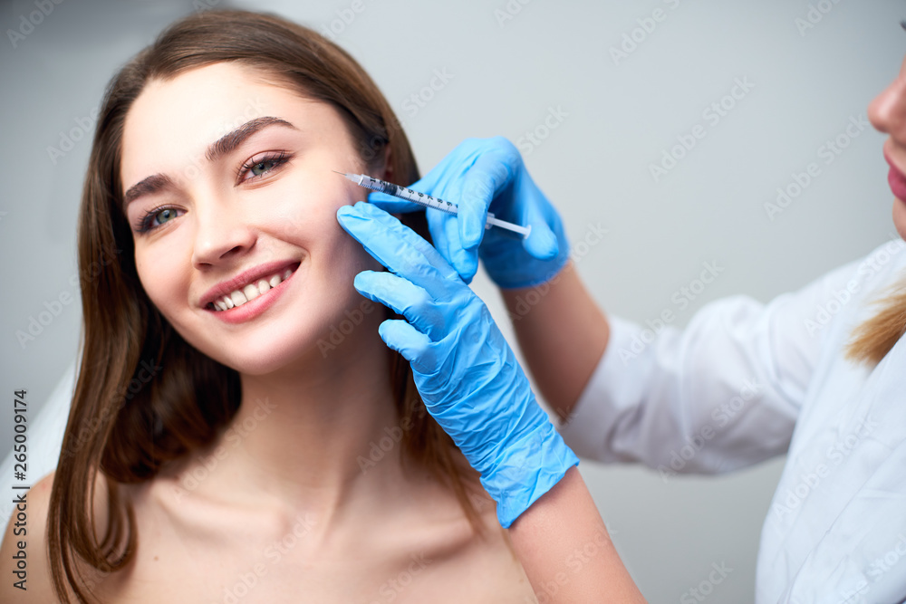 Beautician doctor with botulinum toxin syringe making injection to to remove crow's feet. Cheek volume enhance mesotherapy. Anti-aging treatment and face lift in cosmetology clinic.