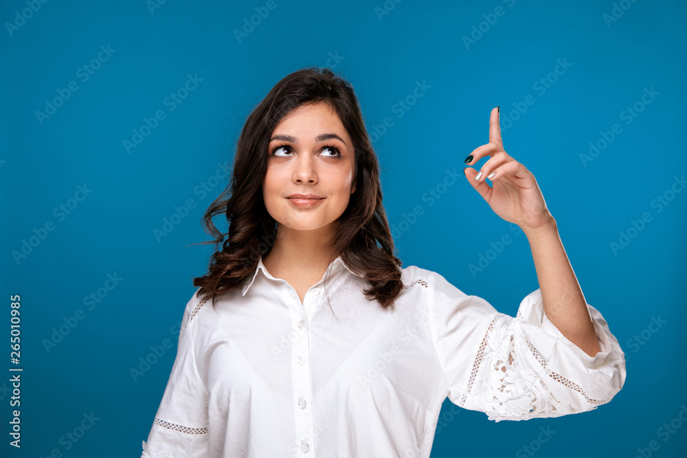 Pretty brunette girl pointing something by finger isolated over the blue background Pretty brunette girl pointing something by finger isolated over the blue background