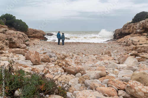 Pareja de enamorados mirándose en una playa de piedras de la costa mediterránea durante una tormenta. Amor y Aventura.