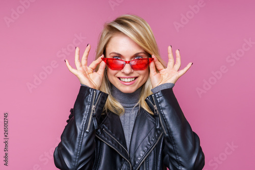 Image of happy blonde in pink glasses and leather jacket with hands near face
