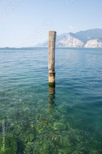 Wooden bricole for boats in the water, lake Lago Di Garda, morning light, mountains on the background © Iva