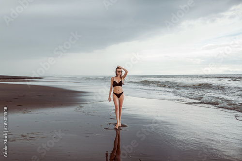 Thin girl in a swimsuit goes on the black beach.