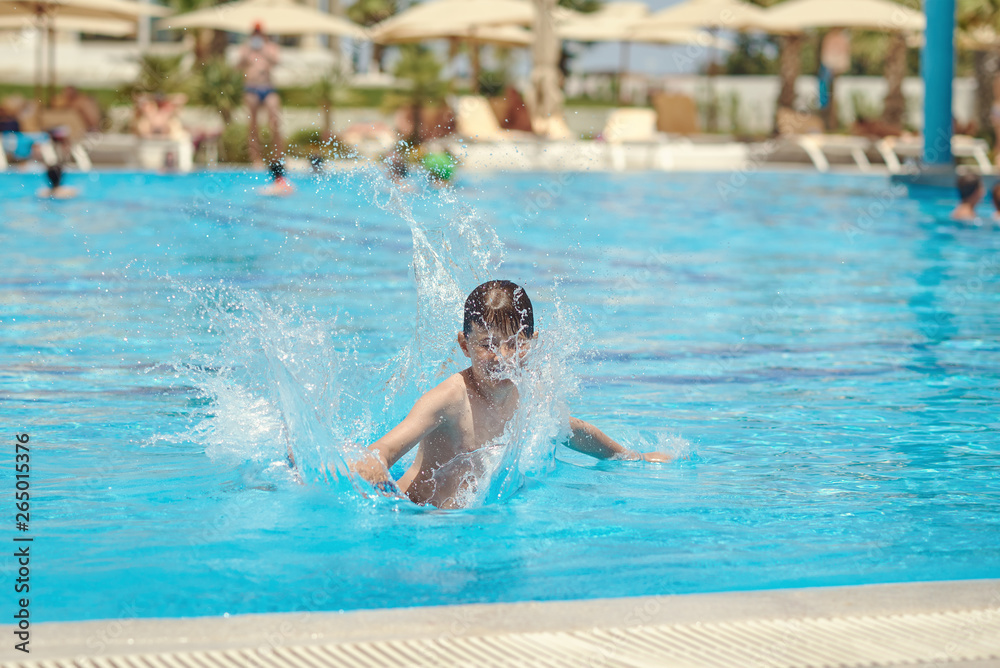 European boy jumping into swimming pool at resort. Moment of entrance in water.