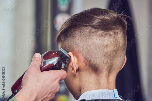 Hairdresser making a haircut to a boy with clipper. Back view.