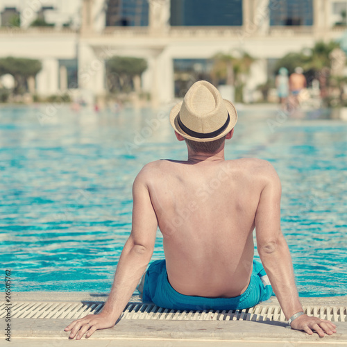 European man in sun hat on side of swimming pool on summer vacation. Back view.