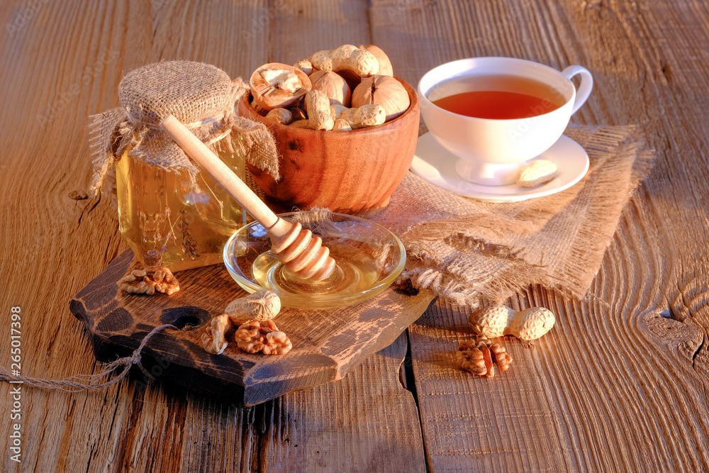 Honey jar, walnuts in a wooden cup, a cup of tea on a wooden table in the sunlight.