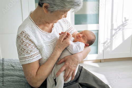 Great-grandmother plays with a newborn great-granddaughter. A grandmother with gray hair is nursing a little granddaughter. Grandmother holding her granddaughter by the handles 