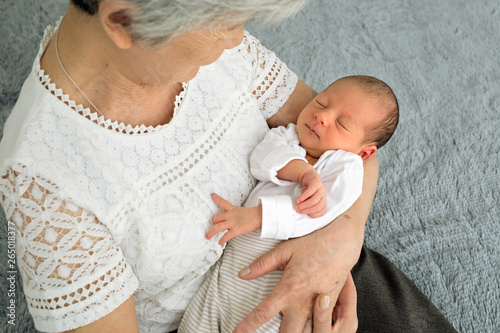 Great-grandmother holds a newborn great-granddaughter in her arms. A grandmother with gray hair is nursing a little granddaughter. Grandmother holding her granddaughter by the handles