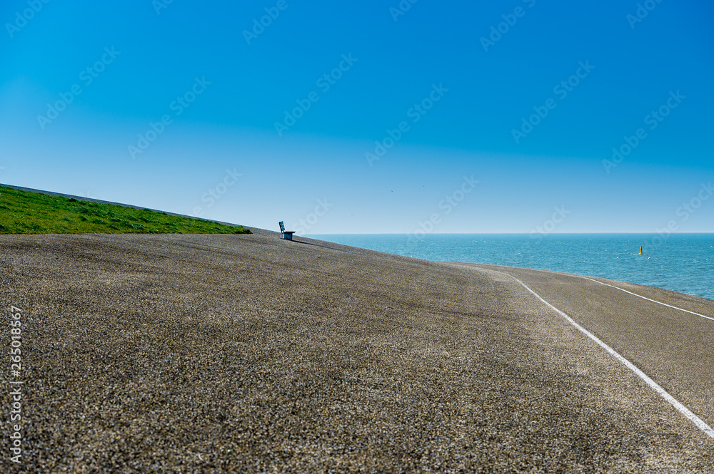 Obraz premium empty bench by sea with green grass and blue sky