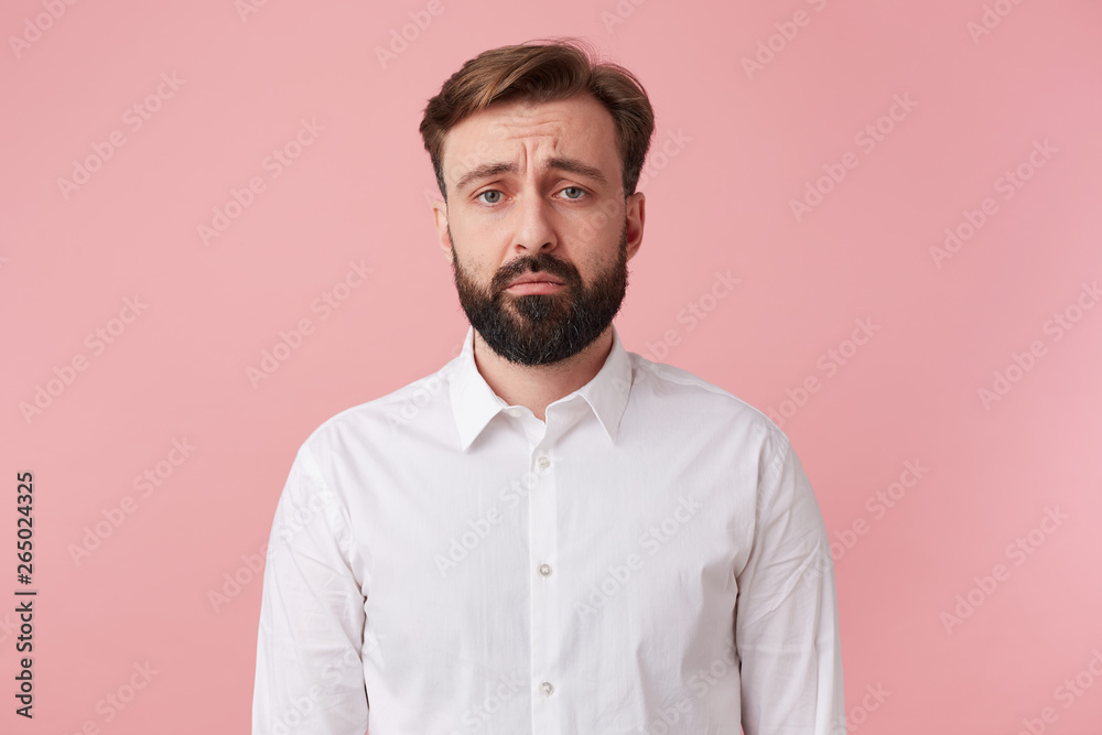 The handsome bearded man frowns and looks sadly at the camera, he was told the news unpleasant. Isolated over pink background. The handsome bearded man frowns and looks sadly at the camera, he was told the news unpleasant. Isolated over pink background.