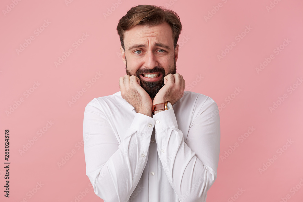 Porterait of young handsome bearded man, with wide open mouth, bites finger nails, scared, isolated over pink backgroundt. Porterait of young handsome bearded man, with wide open mouth, bites finger nails, scared, isolated over pink backgroundt.