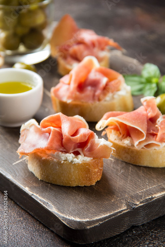 Toast with serrano ham (jamon, prosciutto crudo, hamon), traditional Italian antipasti. Delicious snack with bread, cream cheese, olives. Health food, appetizer for wine, bruschetta