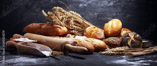 Obraz na płótnie Assortment of baked bread and bread rolls on rustic black bakery table backgroun