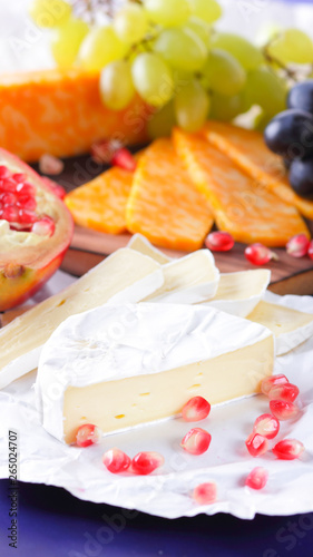 Different types of cheese and fruit. Sliced camembert and pomegranate. Soft and hard cheese and nuts. Camembert and grapes on blue background. Vegetarian food