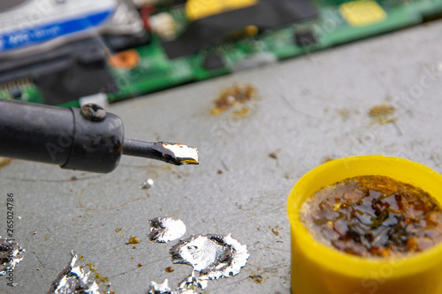 hot smoking soldering iron with rosin and tin, molten metal drops, electronic devices in the background, selective focus, close