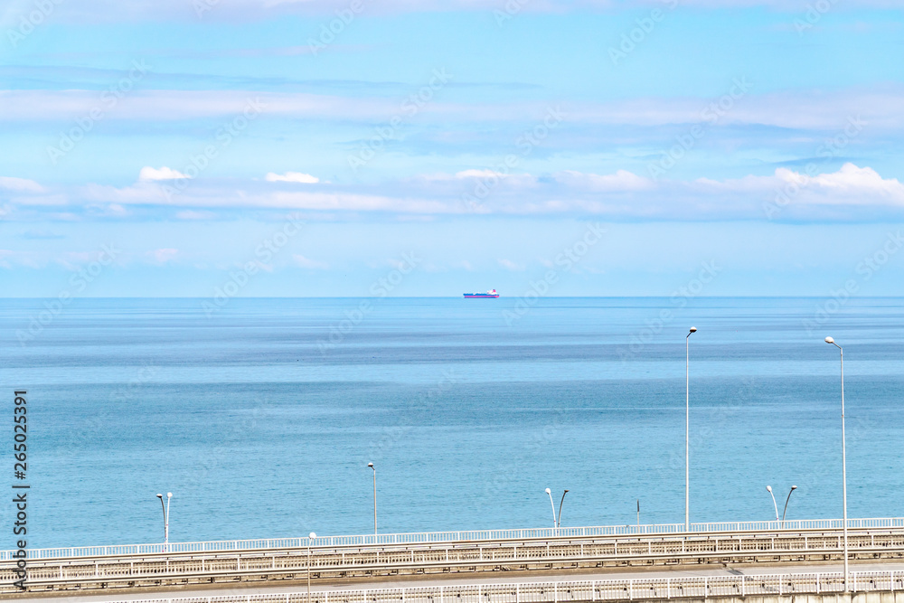Seascape with ship and highway under cloudy sky.