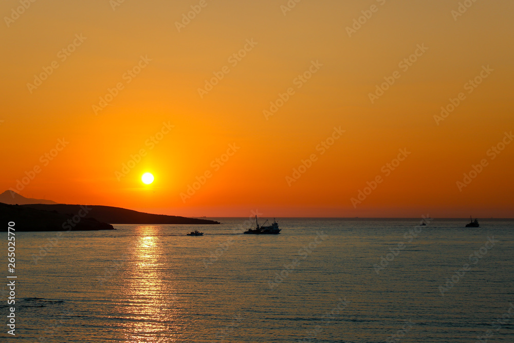 Sunset over the sea. Drifter type (trawler) commercial fishing boats passing in front of the sun and on the way to night fishing. Old Phocaea, Izmir / Turkey.