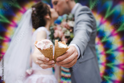 The bride and groom are eating ice cream together on a bright wall background. Funny newlyweds eat ice-cream. Happy Wedding Day