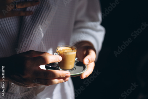 A man in a bathrobe is holding a small mug of coffee