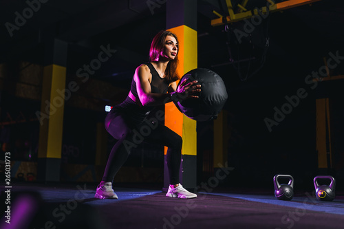 Sportswoman doing squat exercises with fitness ball. Female exercising and stretching with medicine ball at gym.