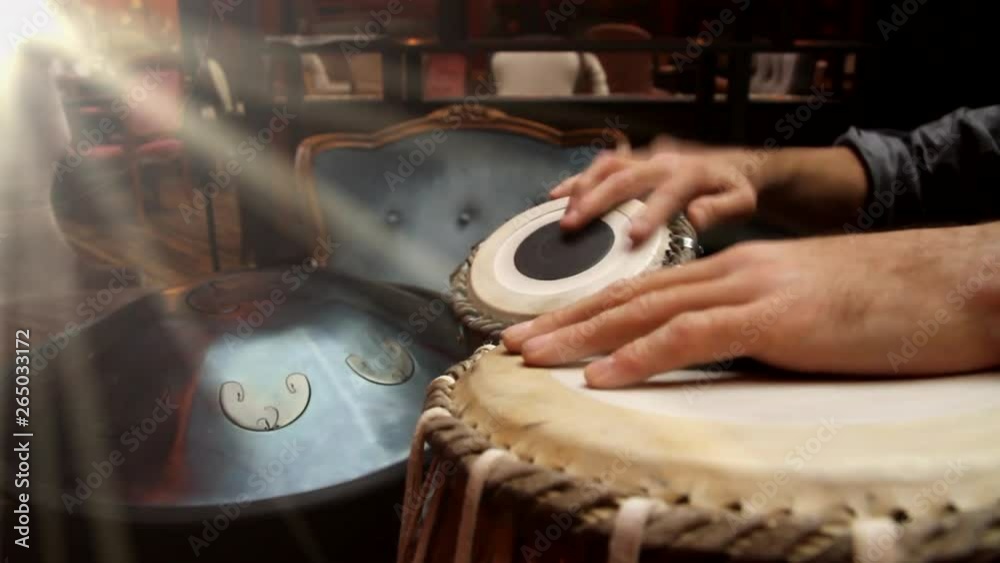 A man playing an ethnic musical instrument tabla in the interior of the lounge, with the rays of the sun from window