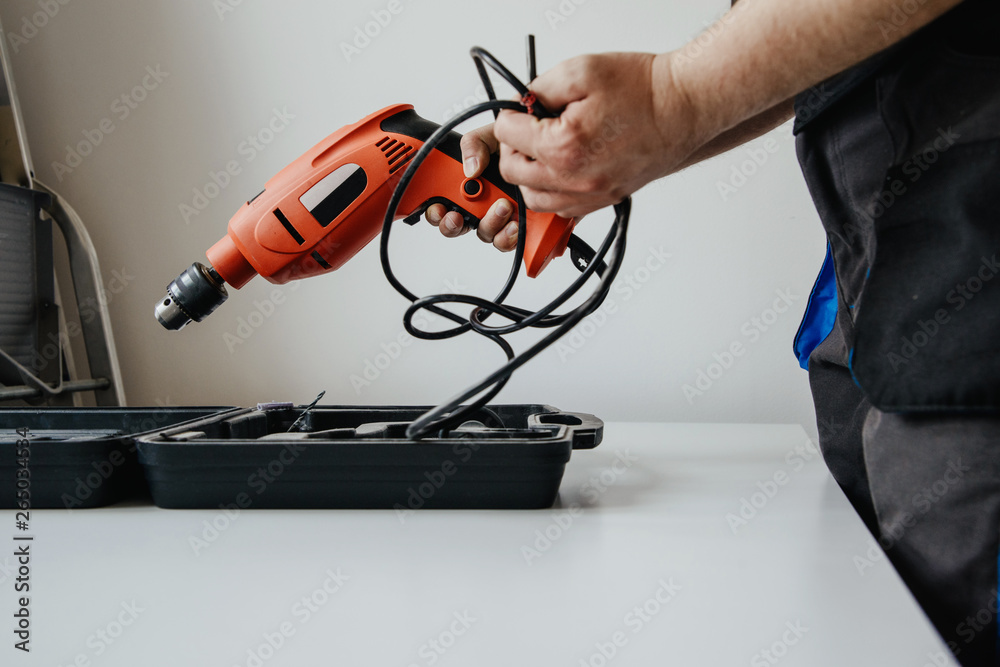 The worker opens the toolbox and pulls out the drill. The concept of work, hiring a professional. Preparing for work, drilling, renovation at home. The worker opens the toolbox and pulls out the drill. The concept of work, hiring a professional. Preparing for work, drilling, renovation at home.