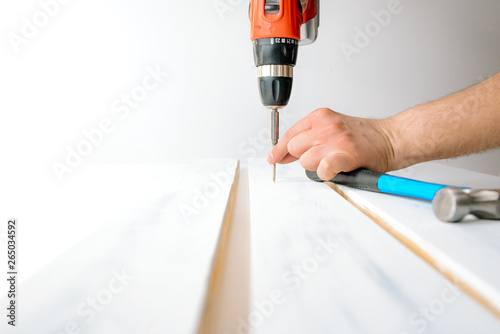 A man screwing a screw into a wooden board. The concept of DIY and renovation of new things. A man tinkering at home, working with wood.